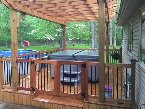 an image of a beautiful backyard and a hot tub installed under a wooden gazebo with a fence and gate