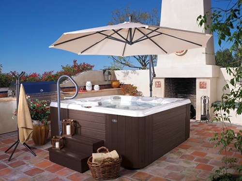 A scene of a beautiful patio with a hot tub in the center and a spa side umbrella overhead on a sunny day